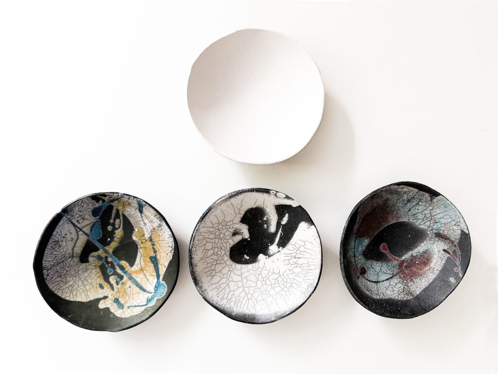 4 bowls places with the first one in the top center, and then the next three lined in a row on the bottom. The 3 bowls below have been raku fired and are examples. The top center bowl is what it looks like before going into the raku fire