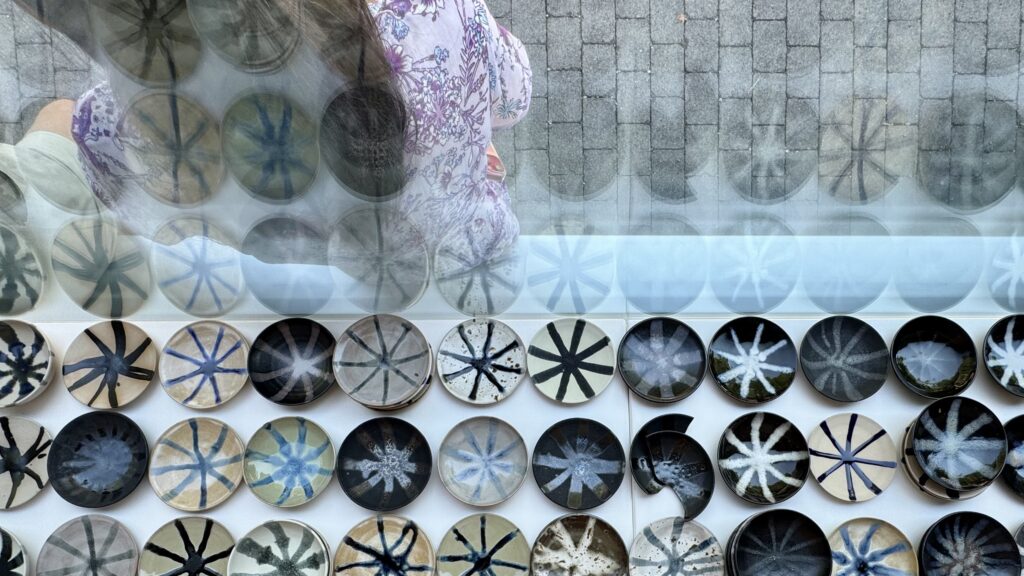 Several ceramic small plates glazed differently, sitting on a window display.