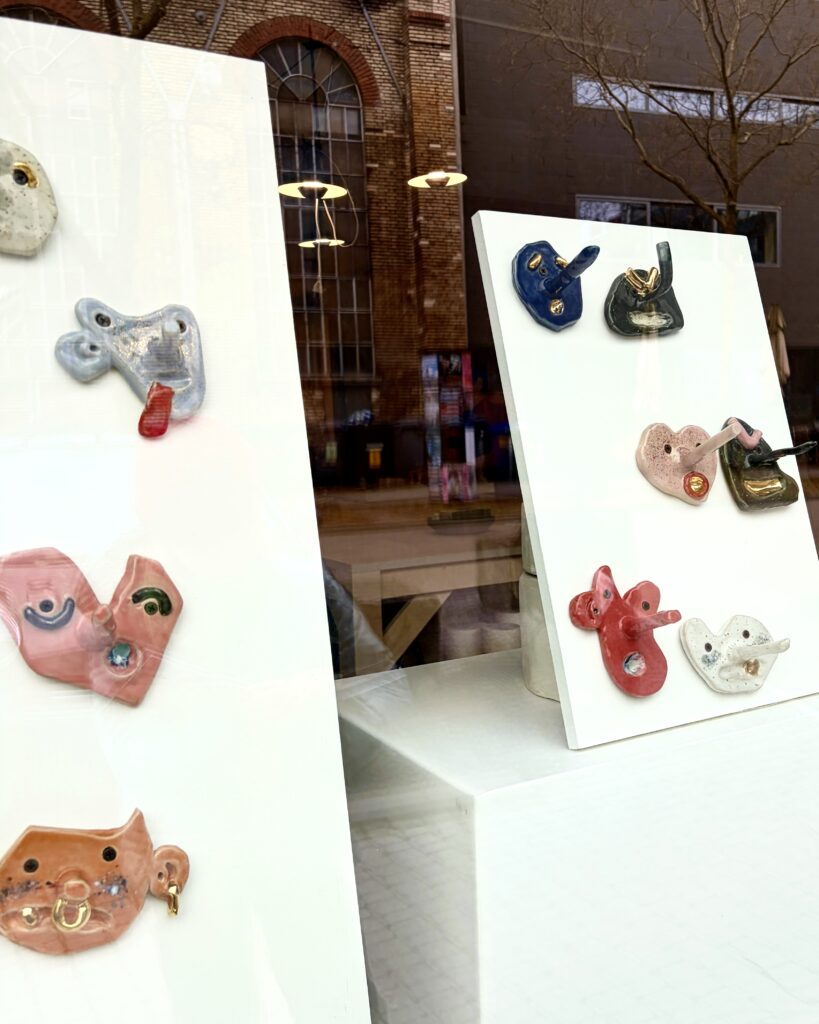 Hand built ceramic monster wall hooks by nine year old maker Moritz Popp displayed in the db pottery studio window, showcasing playful children's pottery with bold colors and expressive faces.