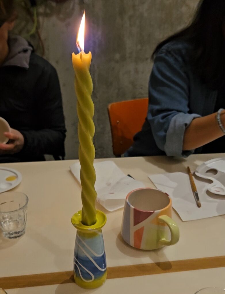 Keramik bemalen mit Farbverlauf und Linien: Glasierter Kerzenhalter mit weichen Blau- und Grüntönen sowie abstrakten weißen Linien, kombiniert mit gedrehter Kerze im Workshop-Setting.