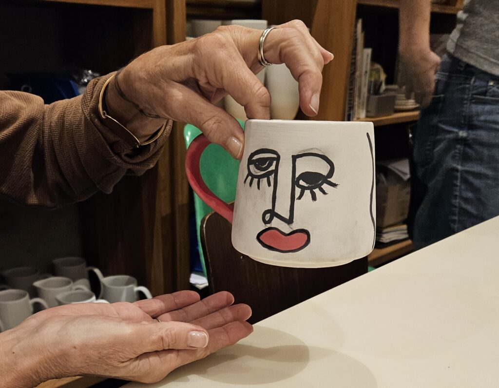 Keramik bemalen mit Linien-Design: Handbemalte Tasse mit minimalistischer schwarzer Gesichtszeichnung und roten Lippen im modernen, grafischen Stil.