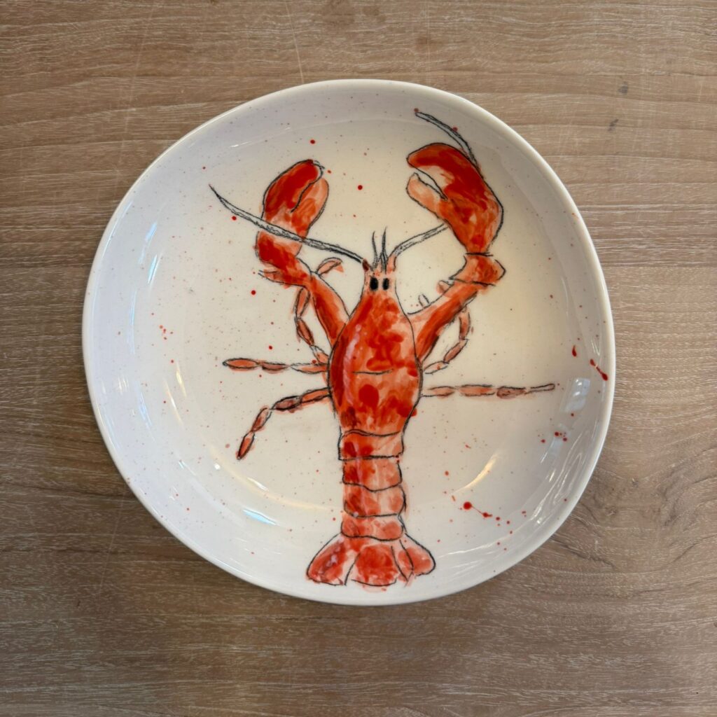 Keramik bemalen mit Spritztechnik: Weißer Teller mit handgemaltem Hummermotiv und roter, zufällig verteilter Splatter-Glasur für einen lebendigen, dynamischen Effekt.