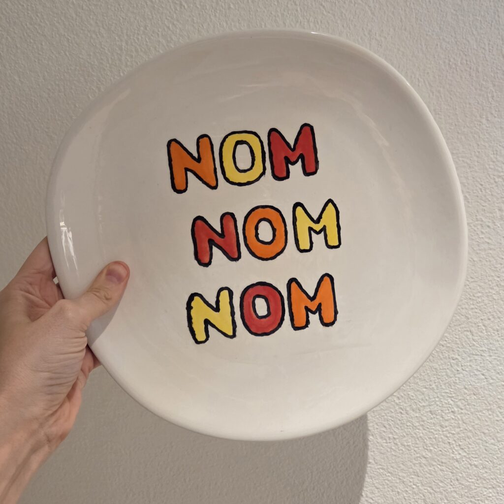 Keramik bemalen mit Schriftzug-Design: Handbemalter Teller mit farbigem „NOM NOM NOM“ Motiv in kräftiger Glasur im modernen Pottery & Paint Stil.