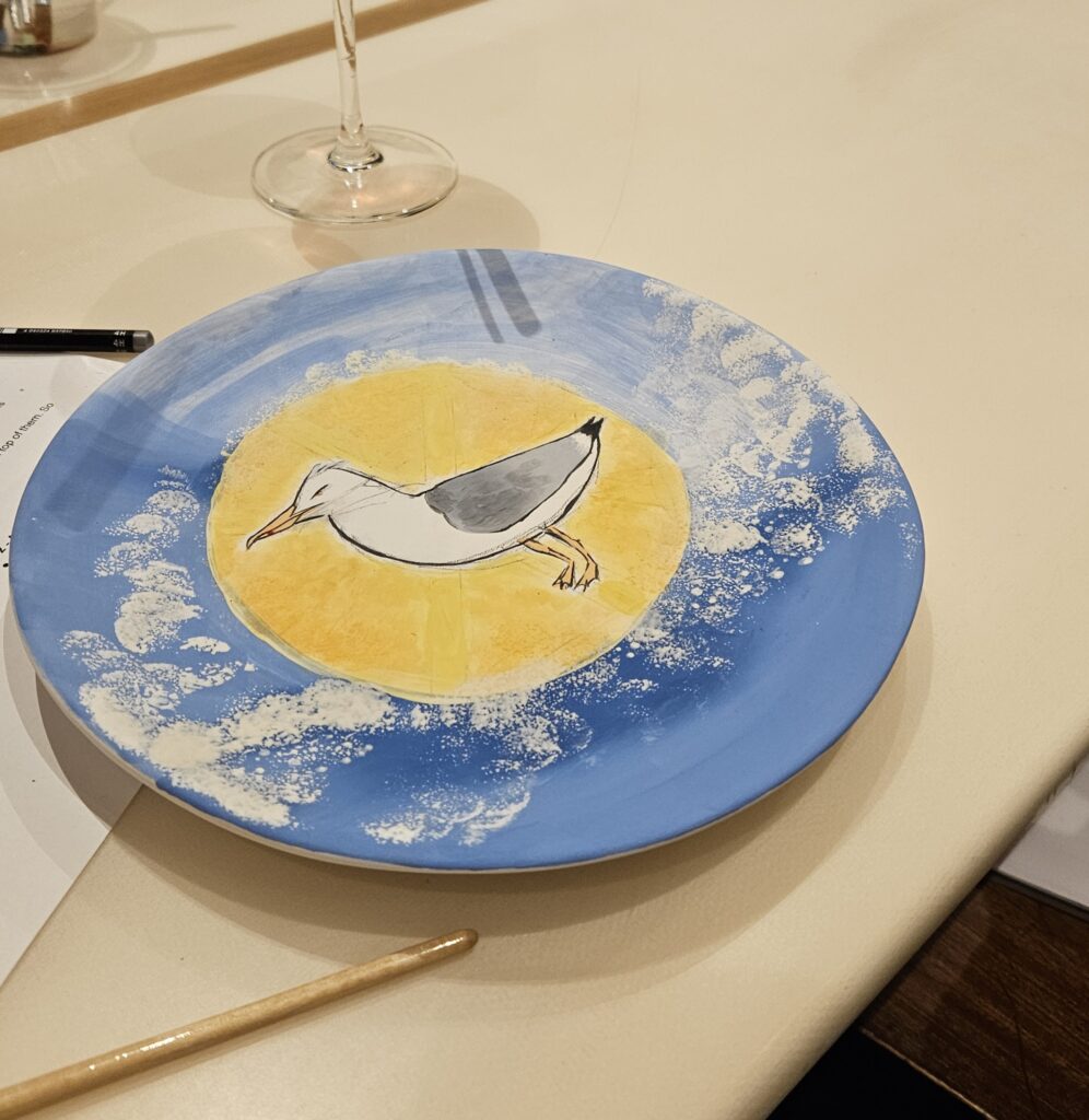 Keramik bemalen mit Schwammtechnik: Teller mit blauem Hintergrund und weißer, getupfter Struktur, kombiniert mit handgemaltem Möwenmotiv im Zentrum.
