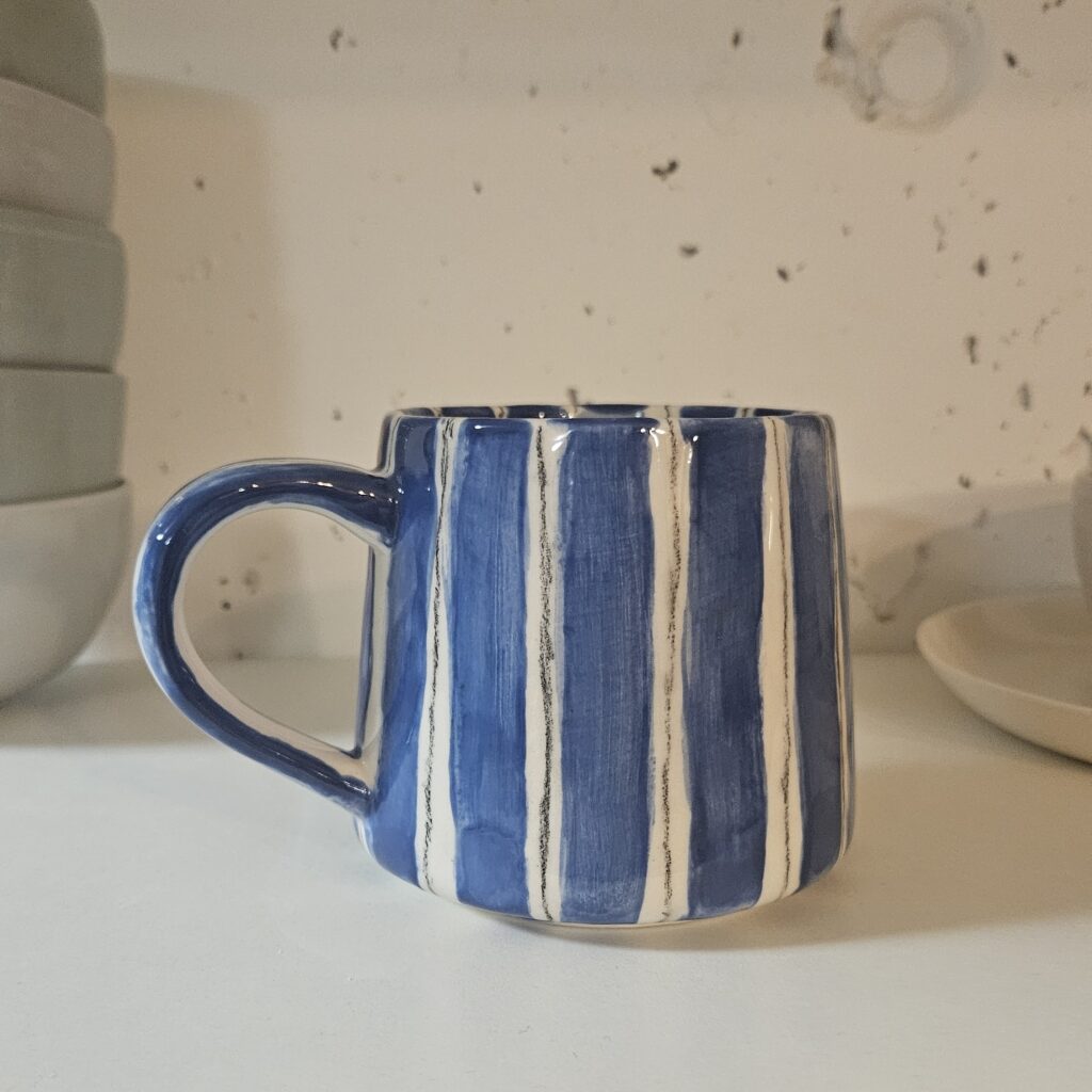 Keramik bemalen mit Streifen-Technik: Handbemalte Tasse mit blauen Glasurstreifen und feinen schwarzen Linien aus Engobe-Stift im modernen, grafischen Stil.