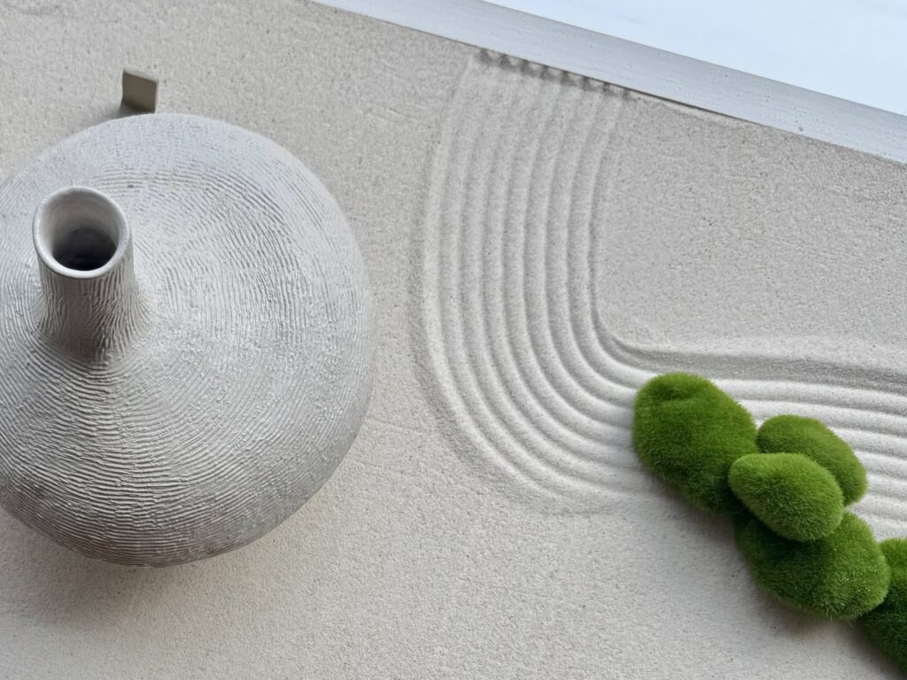 Textured handmade clay vessel with narrow neck on a raked sand surface with green moss, ceramics by Emanuel, Zürich studio