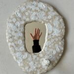 Weisser, ovaler Keramik-Wandspiegel mit strukturierter, blasiger Oberfläche und kleinem rundem Knauf, der eine ausgestreckte Hand spiegelt — Mirror, Mirror Keramik Workshop an den Zurich Design Weeks bei db pottery