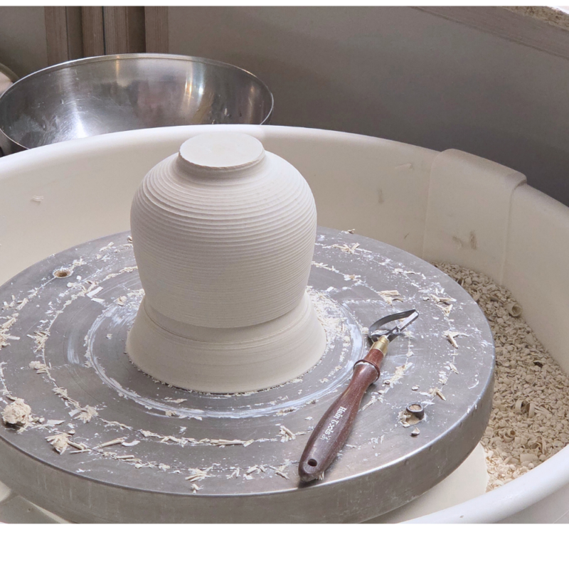 a pottery wheel with a porcelain cup upside down on a chuck ready to be trimmed