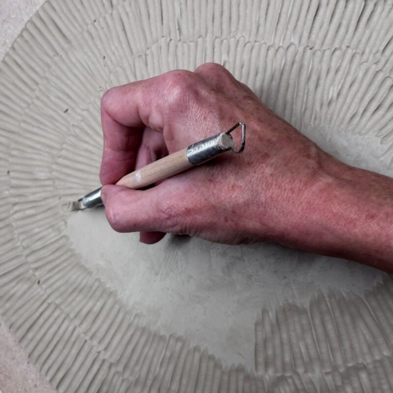 plate being made with clay and a hand carving texture into the clay